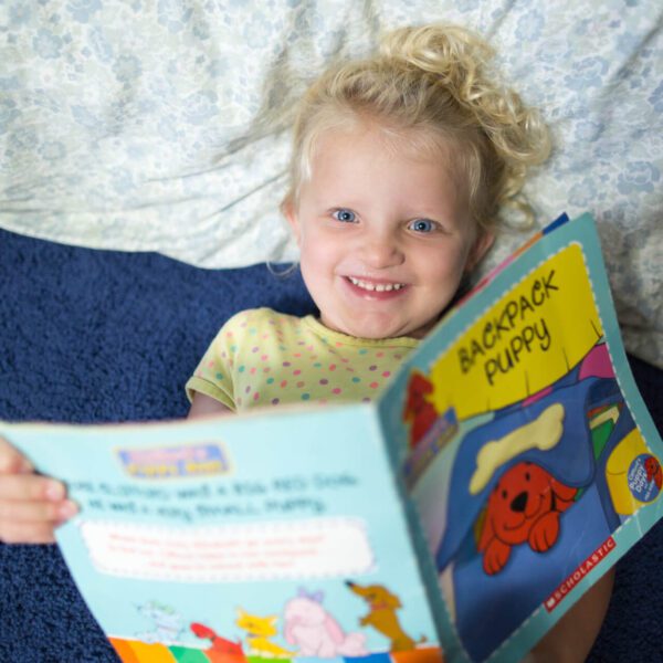 Little girl laying down reading a Clifford book.